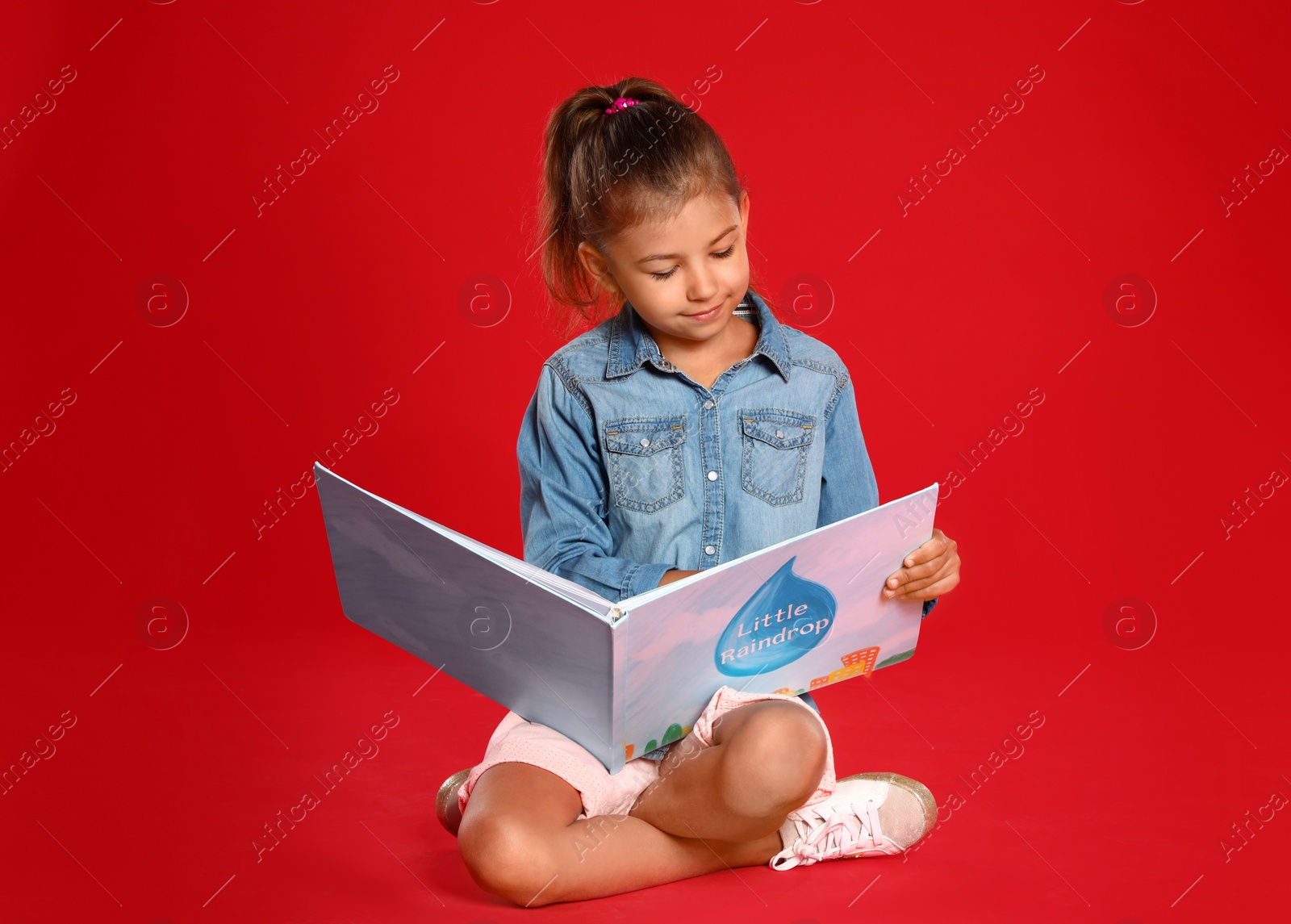 Photo of Cute little girl reading book on red background