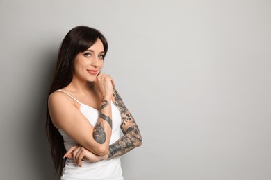 Photo of Beautiful woman with tattoos on arms against grey background. Space for text
