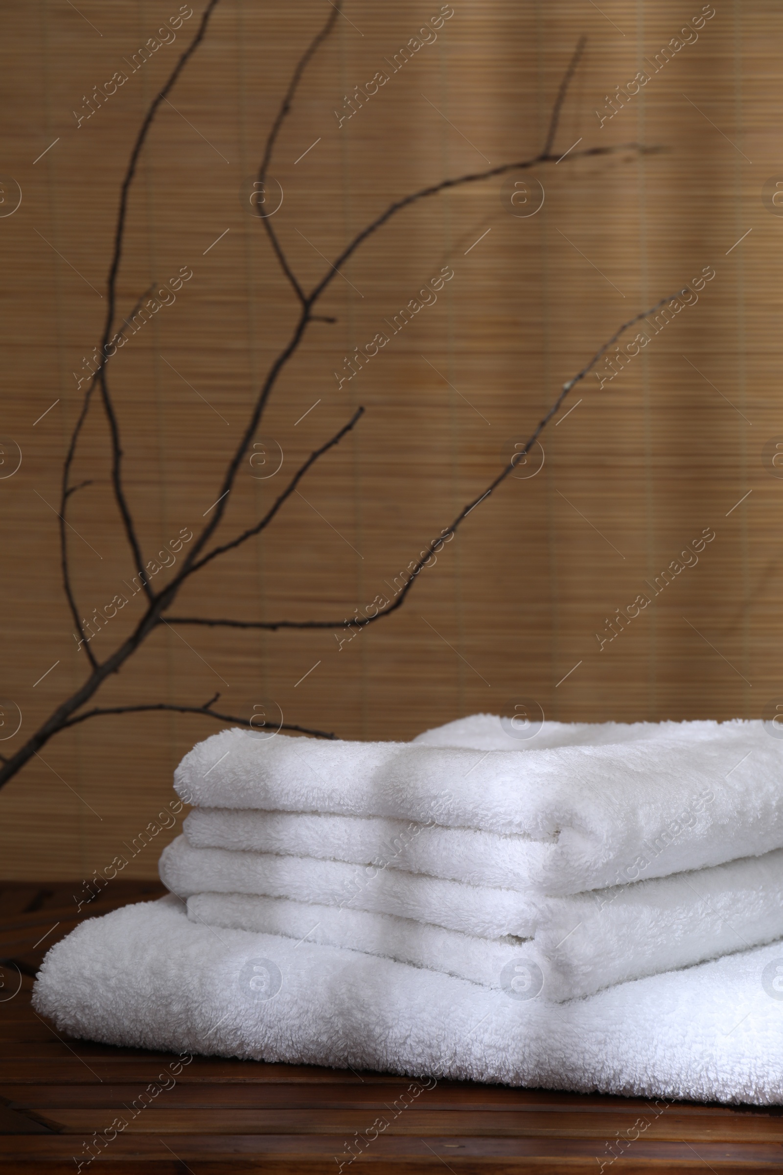 Photo of Stacked soft towels on wooden table and tree branches indoors