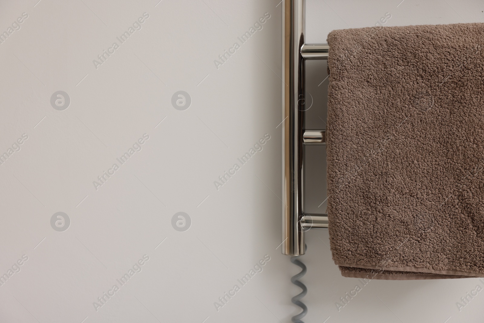 Photo of Heated rail with brown towel on white wall, closeup. Space for text