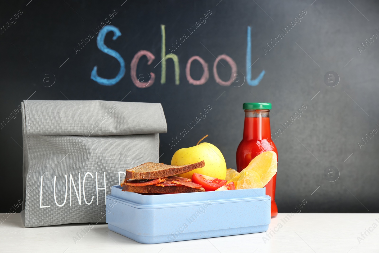 Photo of Appetizing food in lunch box and bag on table near chalkboard with word SCHOOL