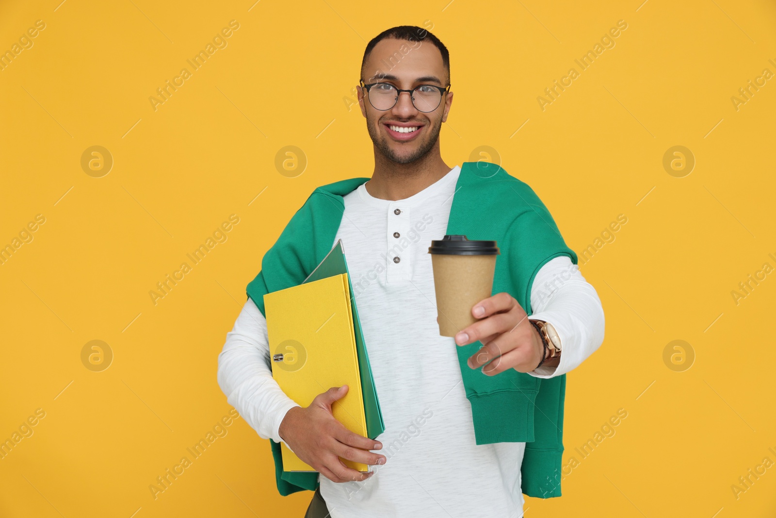 Photo of Happy young intern holding notebooks, cup of hot drink on orange background