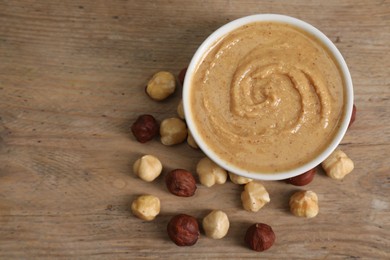 Photo of Delicious nut butter in bowl and hazelnuts on wooden table, top view. Space for text