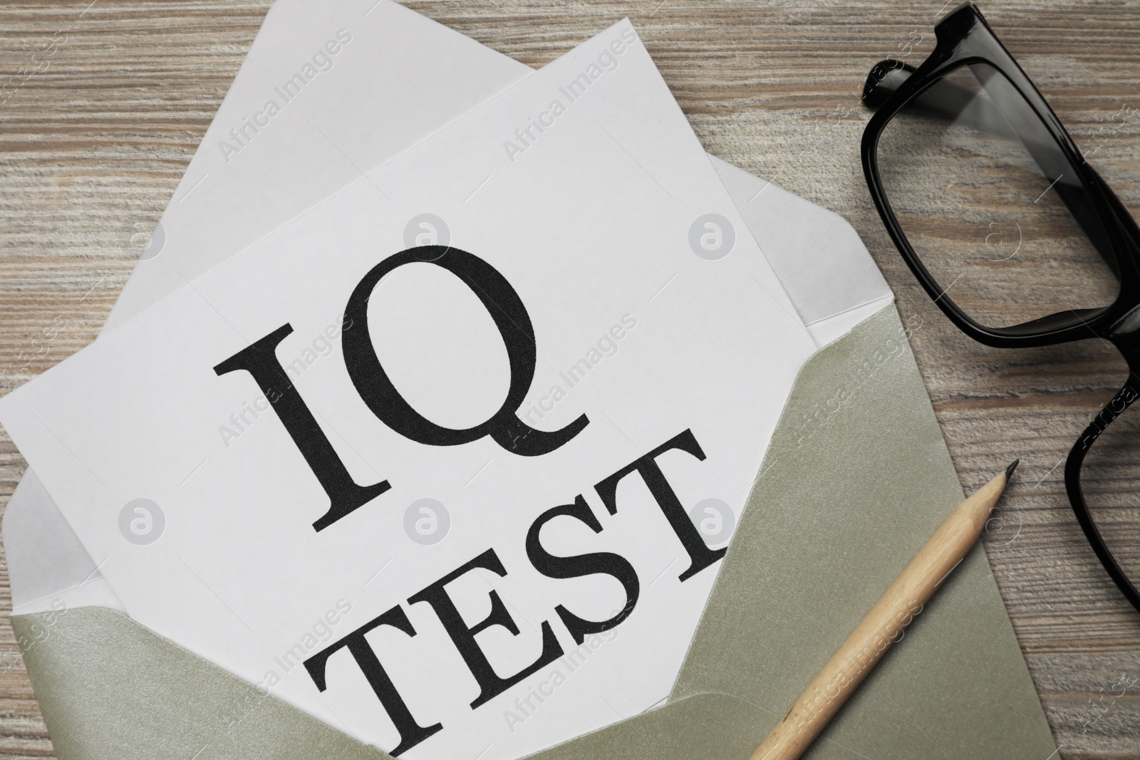 Photo of Paper with words IQ Test in envelope, pencil and glasses on wooden table, flat lay