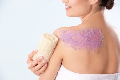 Young woman applying natural scrub on her body against light background
