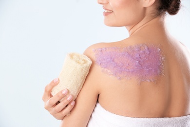 Photo of Young woman applying natural scrub on her body against light background