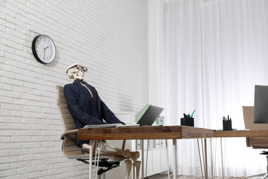 Human skeleton in suit using laptop at table in office