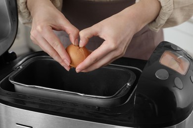 Photo of Making dough. Woman breaking egg into breadmaker pan, closeup