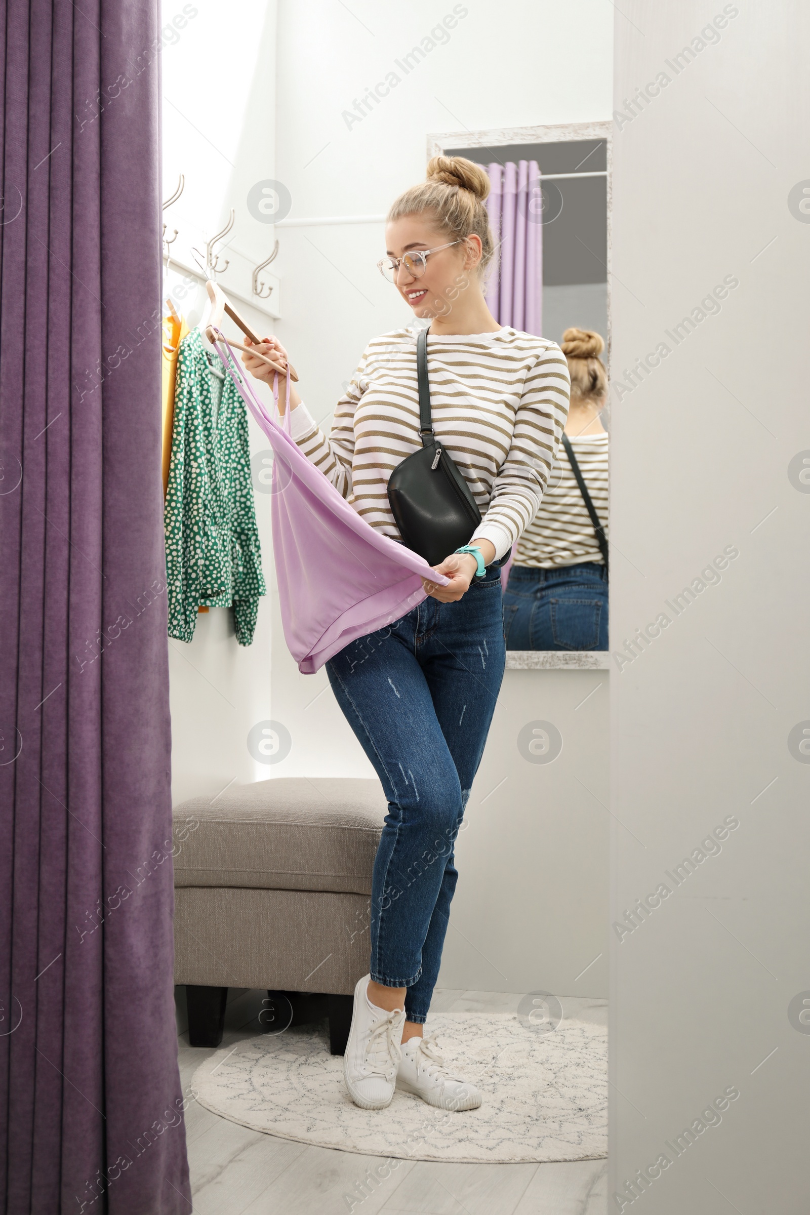 Photo of Young woman with clothes on hanger in dressing room. Fashion store