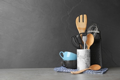 Photo of Holder with kitchen utensils on table against dark background. Space for text