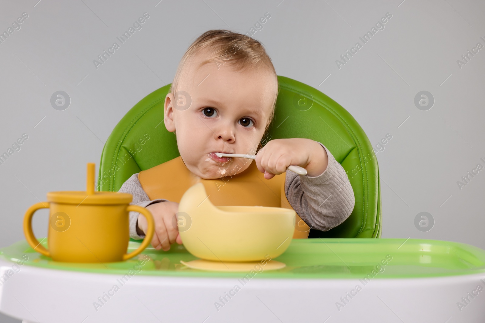 Photo of Cute little baby eating healthy food in high chair on gray background