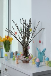 Beautiful pussy willow branches with paper eggs in vase and Easter decor on white chest of drawers at home
