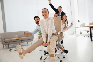 Photo of Happy office employees riding chairs at workplace