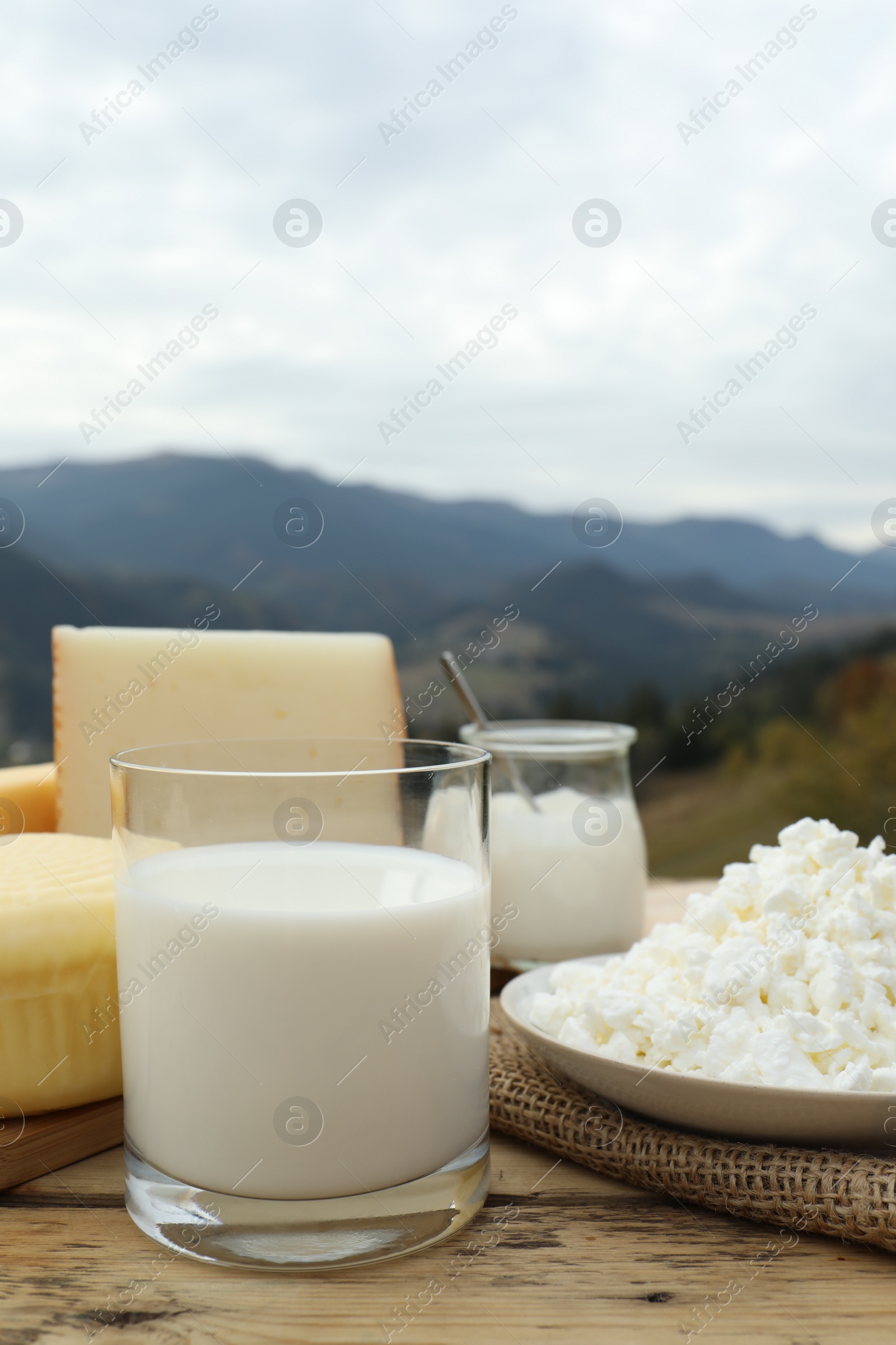 Photo of Tasty cottage cheese and other fresh dairy products on wooden table in mountains