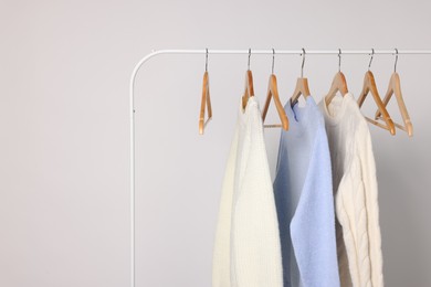 Photo of Rack with different warm sweaters on light background. Space for text