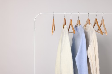 Rack with different warm sweaters on light background. Space for text