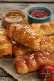 Delicious sausage rolls and ingredients on wooden table, closeup