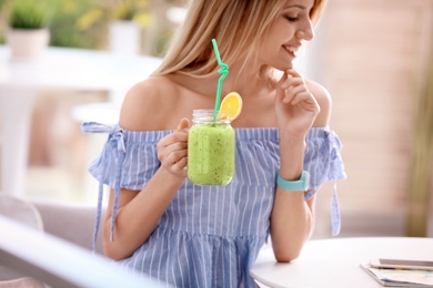 Young woman with tasty healthy smoothie at table, indoors