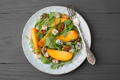 Photo of Tasty salad with persimmon, blue cheese and walnuts served on grey wooden table, top view