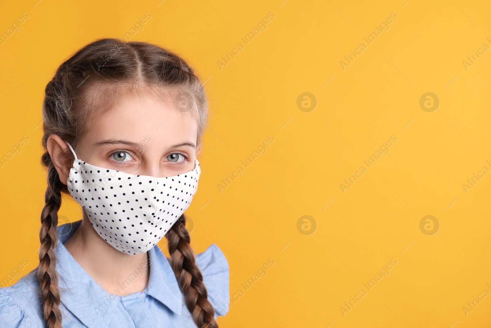 Photo of Girl wearing protective mask on yellow background, space for text. Child's safety from virus