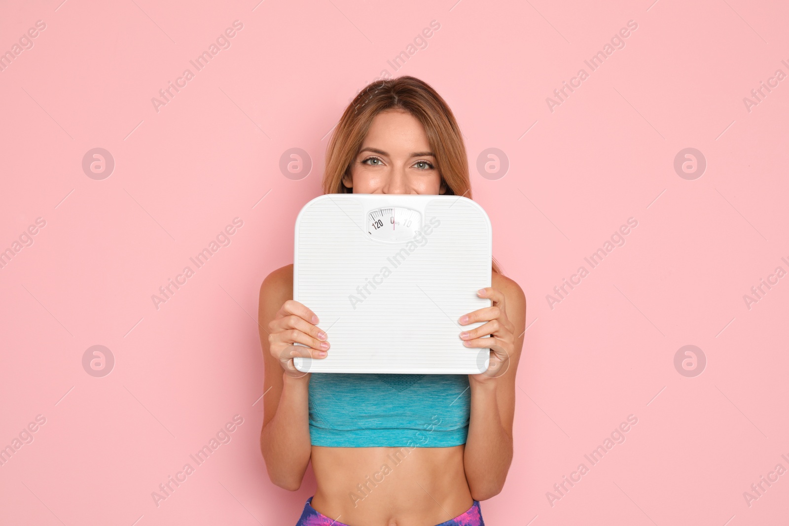 Photo of Happy slim woman satisfied with her diet results holding bathroom scales on color background