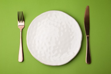 Photo of Clean plate with cutlery on green background, flat lay