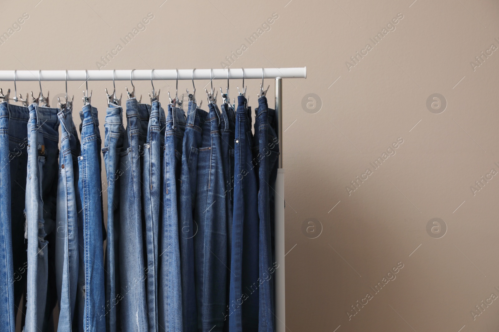 Photo of Rack with stylish jeans on beige background, closeup