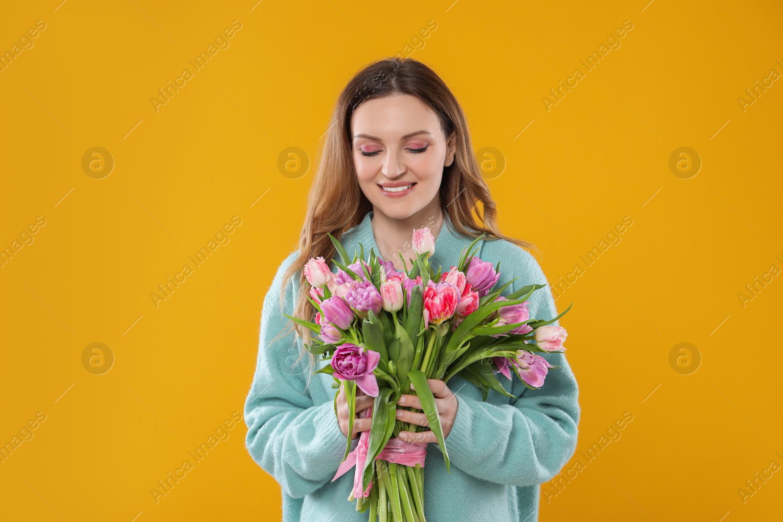 Photo of Happy young woman with bouquet of beautiful tulips on yellow background