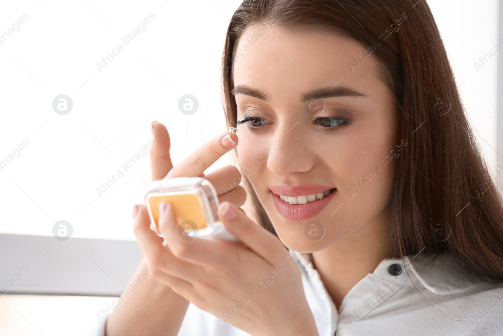 Photo of Young woman putting contact lens in her eye on light background