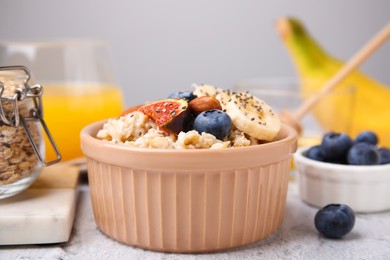 Bowl of oatmeal with blueberries, almonds, banana and fig pieces on white table, closeup