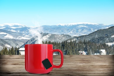 Image of Cup of hot tea on wooden table and beautiful winter landscape on background