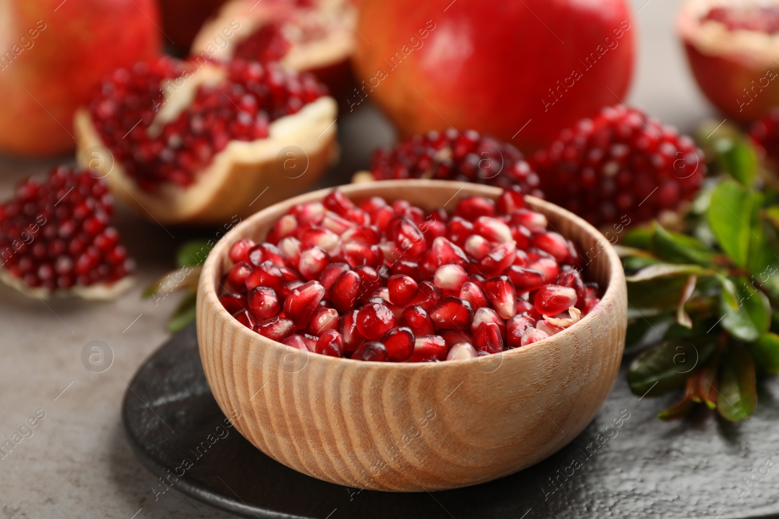Photo of Delicious ripe pomegranate kernels in bowl on grey table, closeup