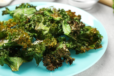 Tasty baked kale chips on light grey table, closeup