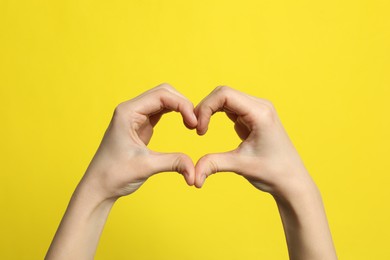 Photo of Woman making heart with her hands on yellow background, closeup