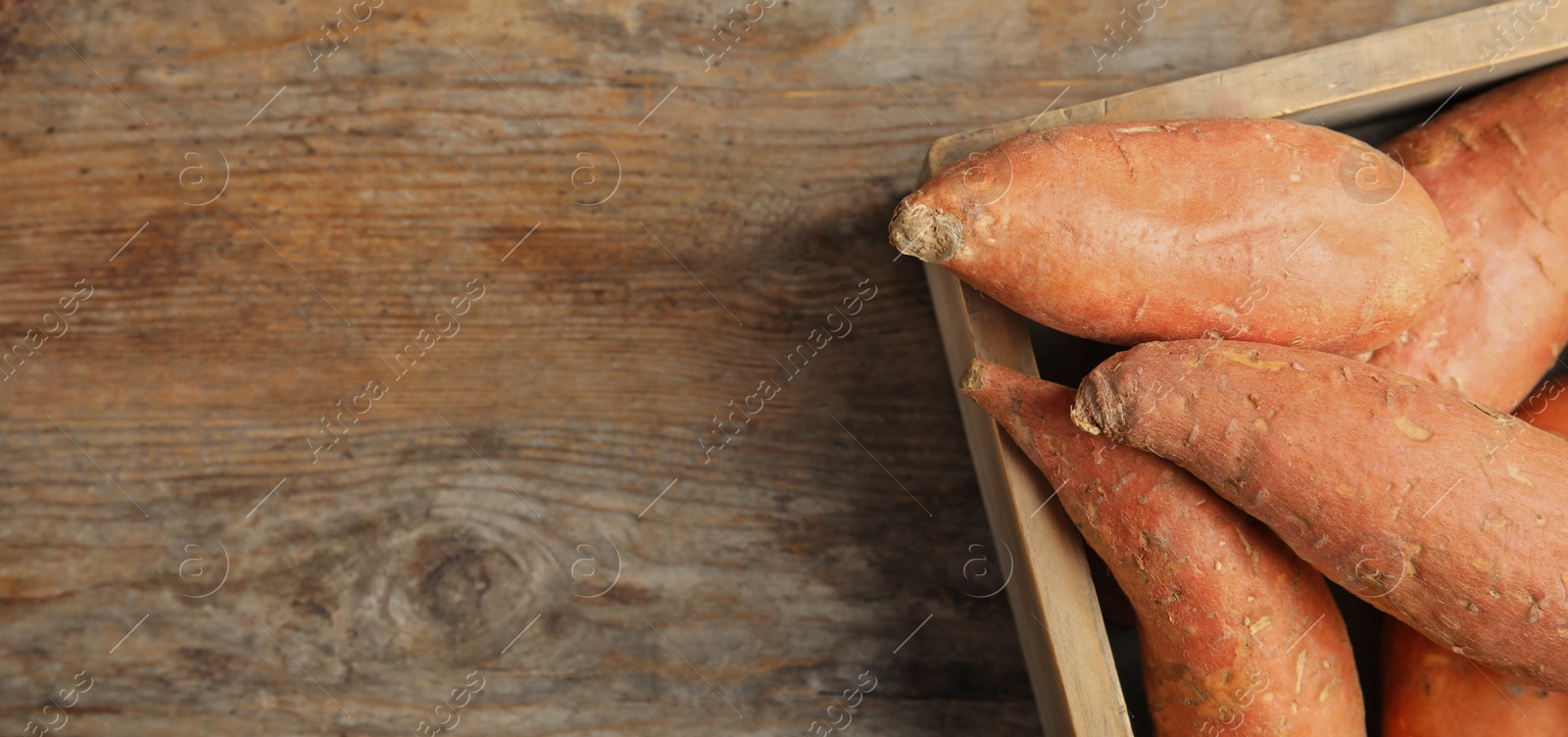 Image of Crate with sweet potatoes and space for text on wooden table, top view. Banner design