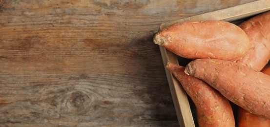 Crate with sweet potatoes and space for text on wooden table, top view. Banner design