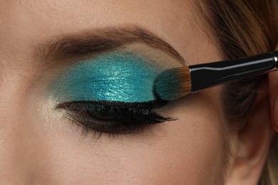 Photo of Applying cyan eye shadow onto woman's face, closeup. Beautiful evening makeup