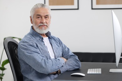 Photo of Handsome senior man working on computer at table in office. Space for text