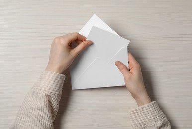 Photo of Woman taking card out of letter envelope at light wooden table, top view