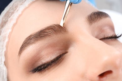 Young woman having professional eyebrow correction procedure in beauty salon