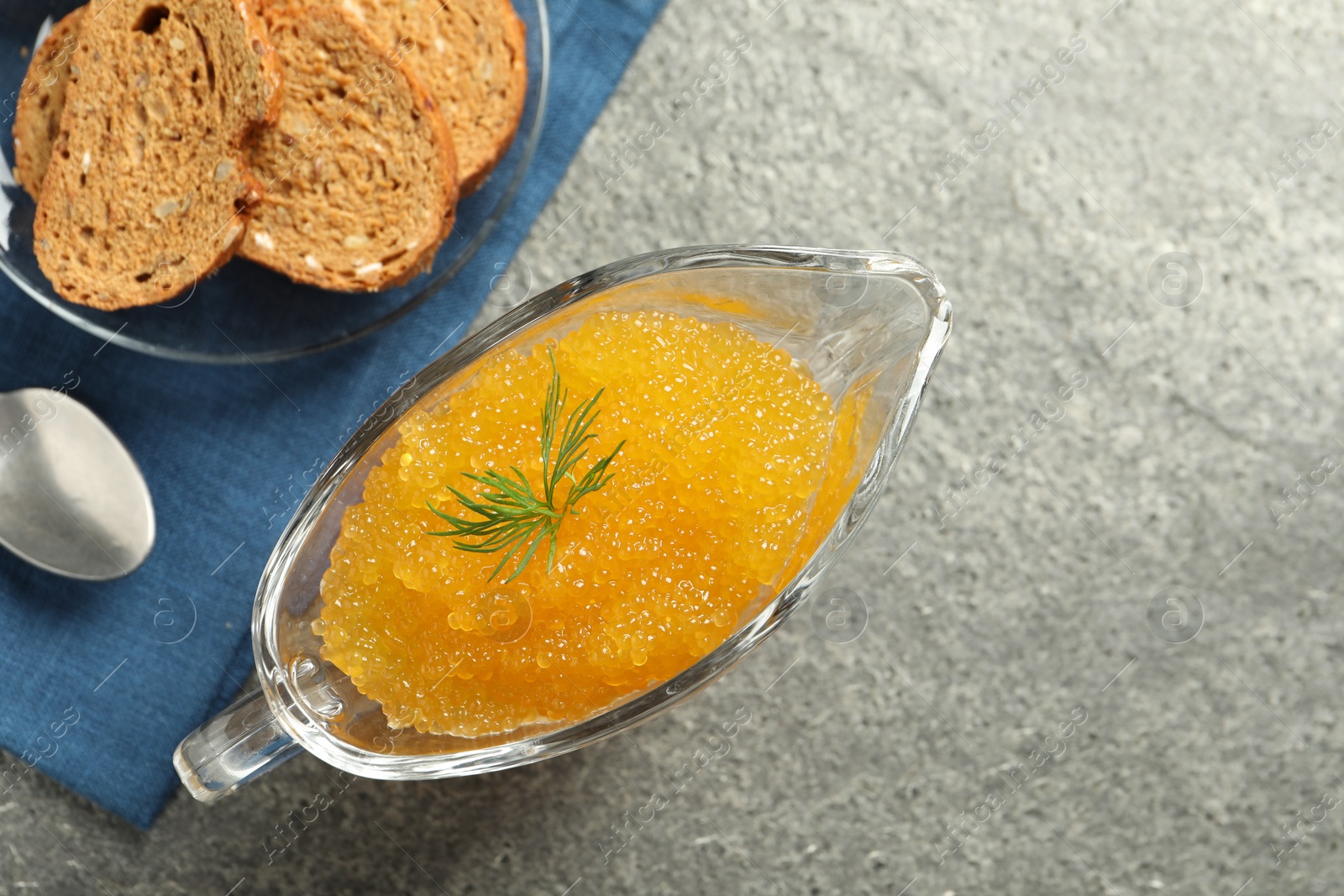 Photo of Fresh pike caviar in gravy boat, bread and spoon on grey table, top view. Space for text