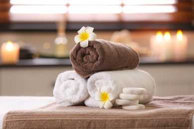 Photo of Composition with towels, flowers and stones on massage table in spa salon