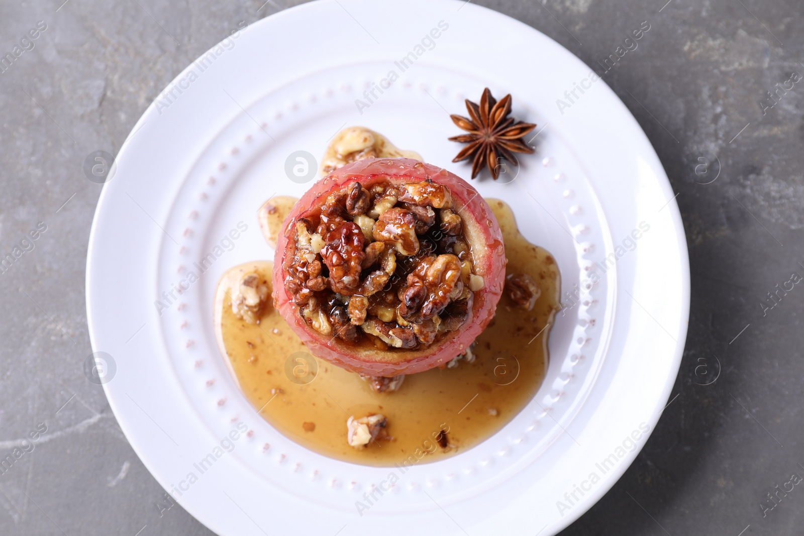 Photo of Tasty baked apple with nuts, honey and anise on gray textured table, top view