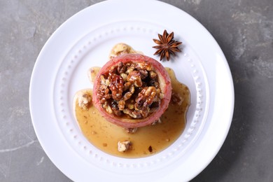 Photo of Tasty baked apple with nuts, honey and anise on gray textured table, top view