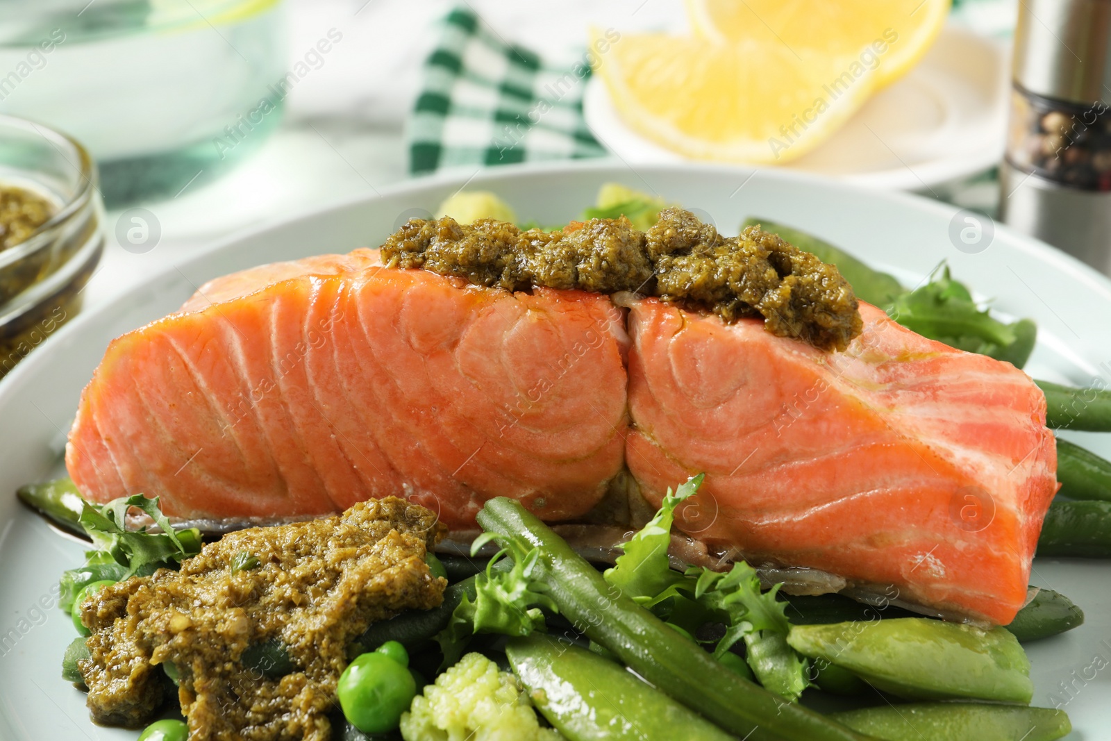 Photo of Tasty cooked salmon with pesto sauce and fresh salad on plate, closeup