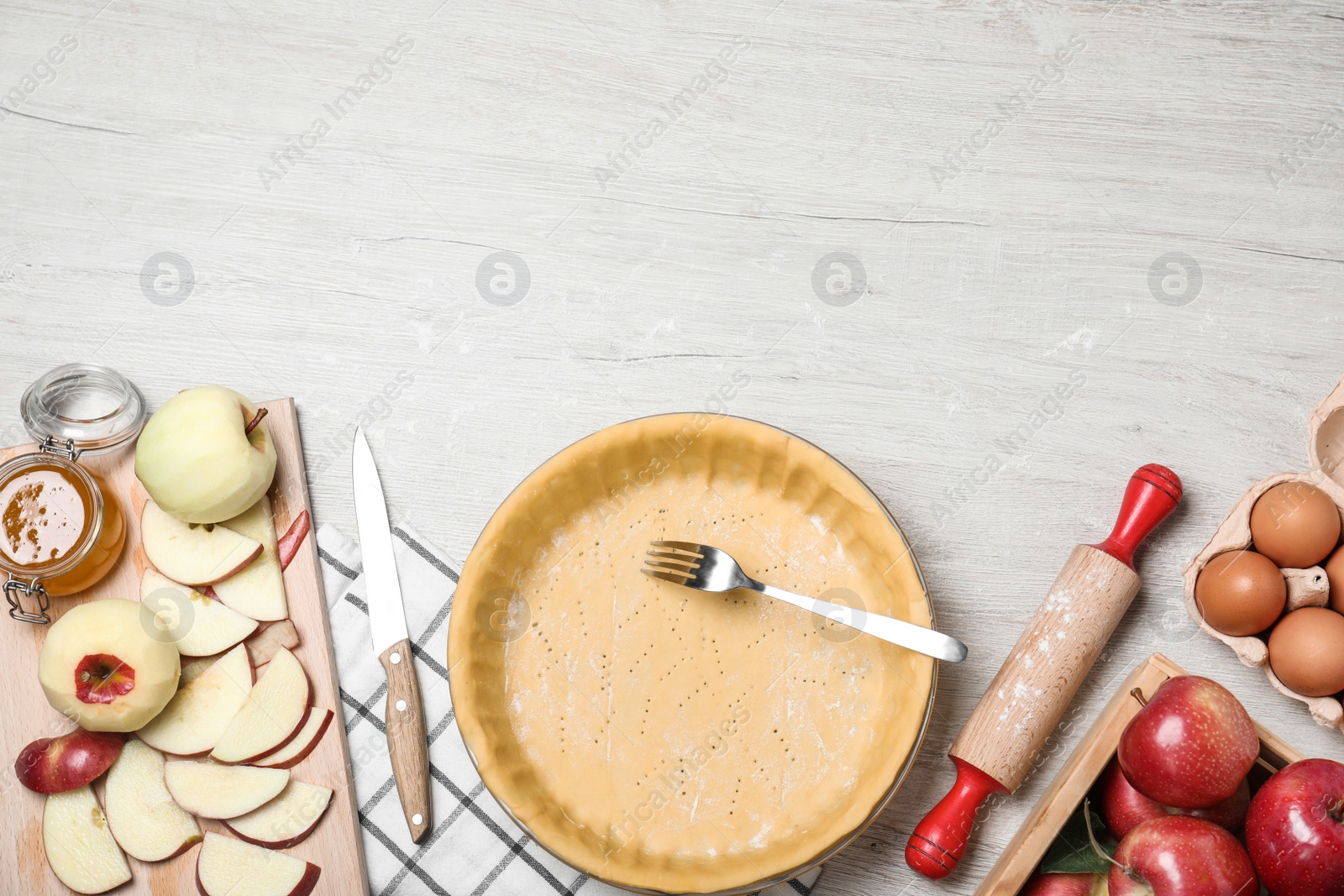 Photo of Flat lay composition with raw dough, fork and ingredients on white wooden table, space for text. Baking apple pie