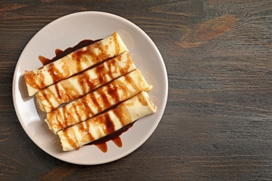 Photo of Thin pancakes served with chocolate syrup on plate, top view