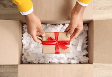 Photo of Man putting Christmas gift box into parcel at wooden table, top view. Sending present by mail