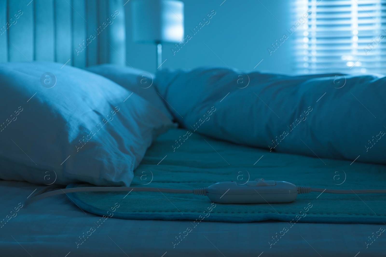 Photo of Bed with electric heating pad indoors at night