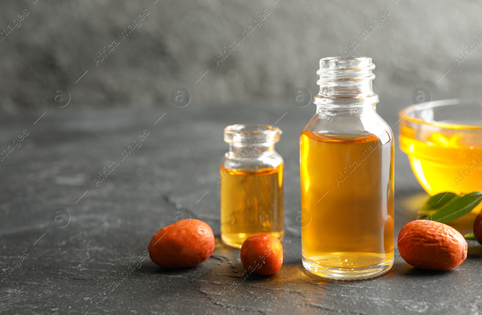 Photo of Jojoba oil and seeds on dark grey table